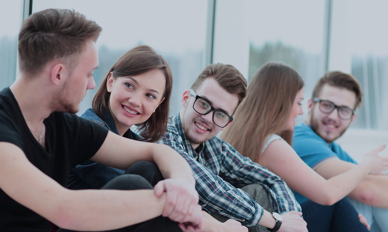 A group of happy students sitting on a window sill and smiling