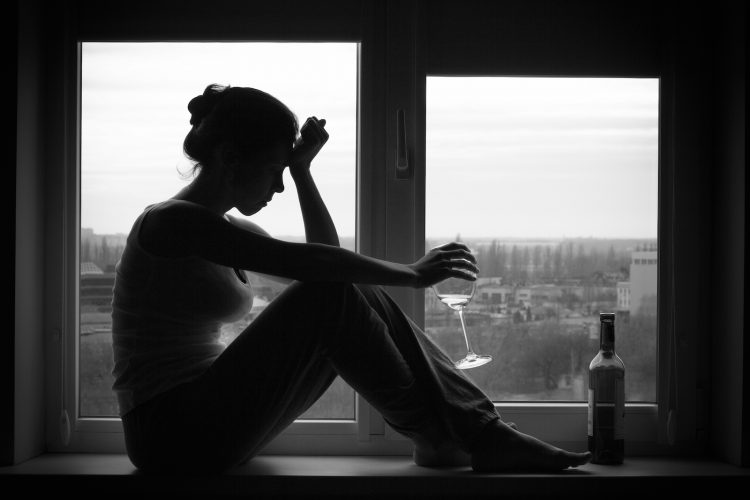 Sad young woman sitting on the window drinks wine. Alcoholism problem. Black and white photography.