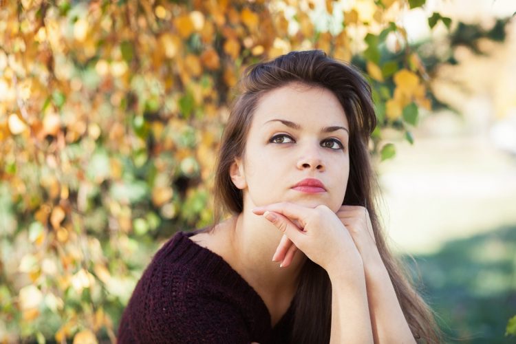 Young woman sitting outside looking off, deep in thought