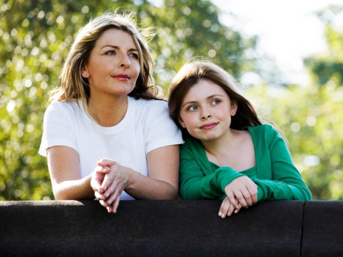 Mother and teen daughter stand on a bridge and talk about positive body image