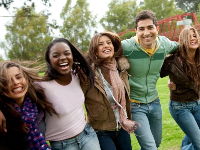 A group of smiling friends standing arm-in-arm on the grass outside