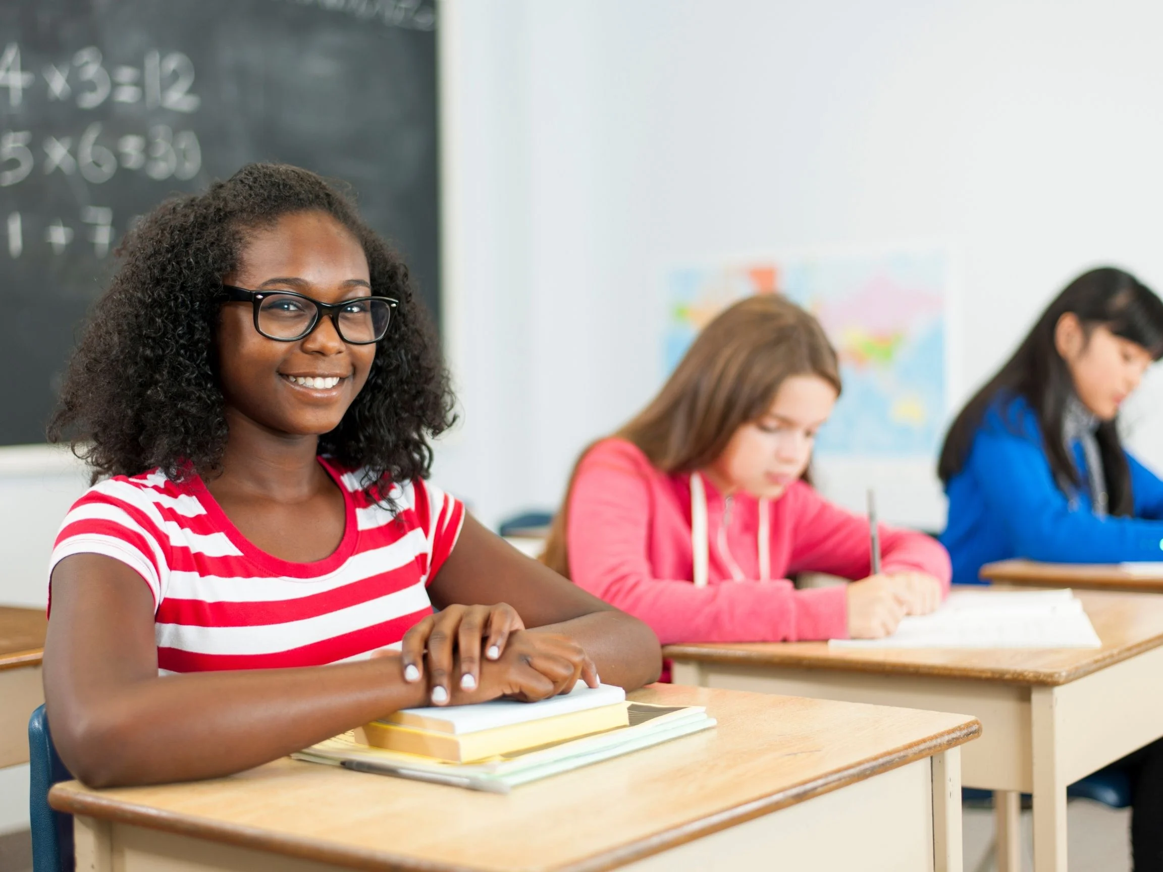 Three female middle school students sit at their desks working on an assignment