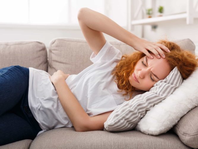 A woman lies on her couch feeling sick from drunkorexia symptoms