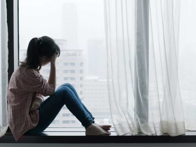 A sad young woman sits at a window