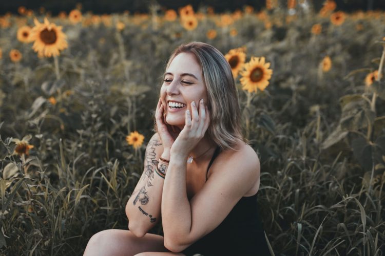 Portrait of a young woman sitting in a field of sunflowers smiling