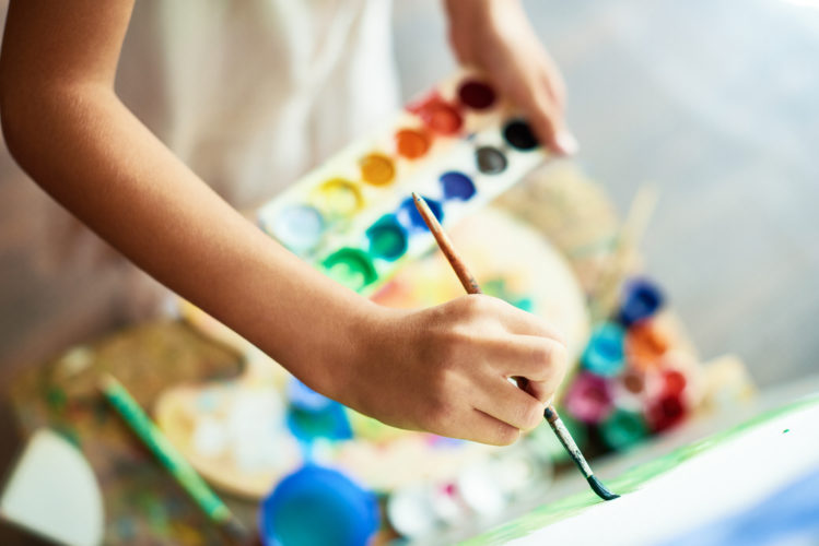 Close-up shot of highly gifted little artist drawing with watercolors on canvas, blurred background