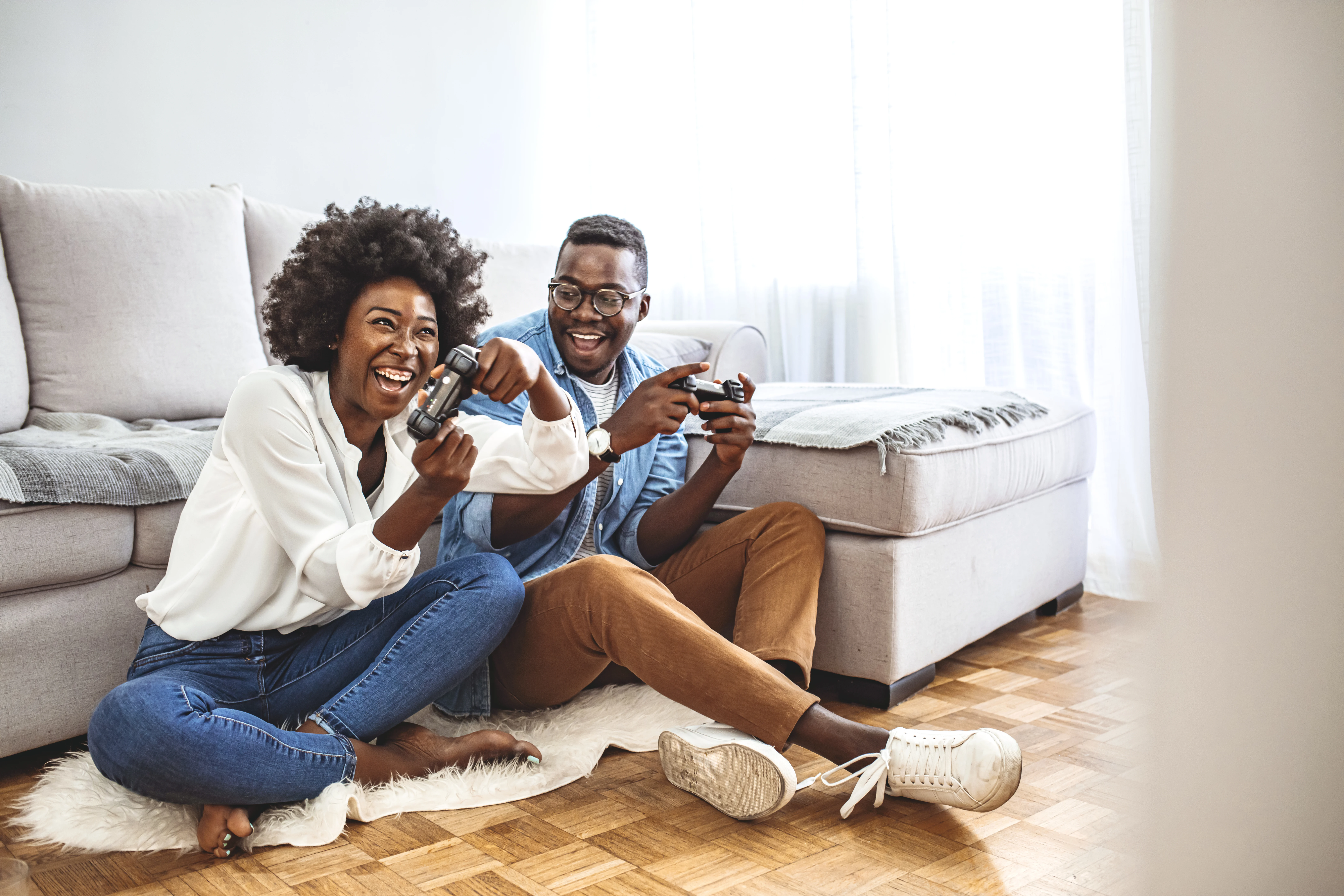 Playing video games. Who will win? Excited funny friends, playing video games at home, sitting on sofa and enjoying themselves. They have great weekend in nice company indoors