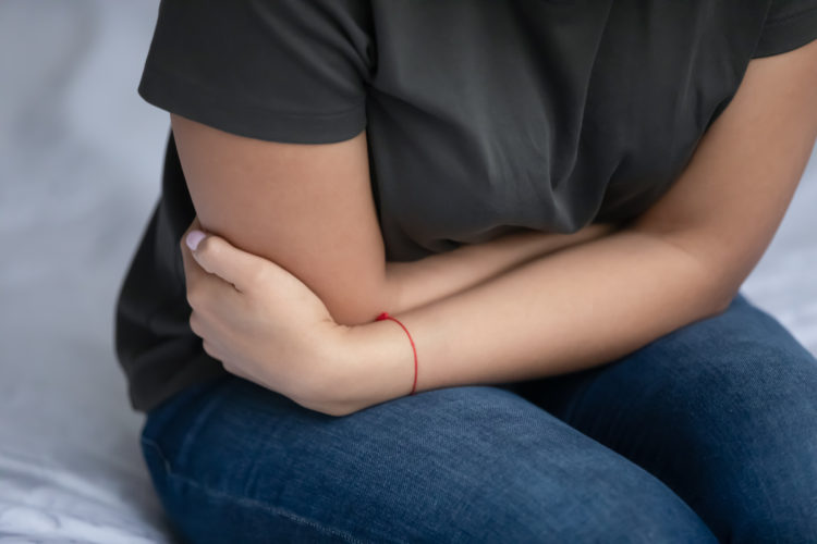 Close up view young woman sit in bed curled up in pain feeling stomachache caused by indigestion, gallstones or painful menstrual period. Gas, appendicitis, ulcers, gastritis need treatment concept