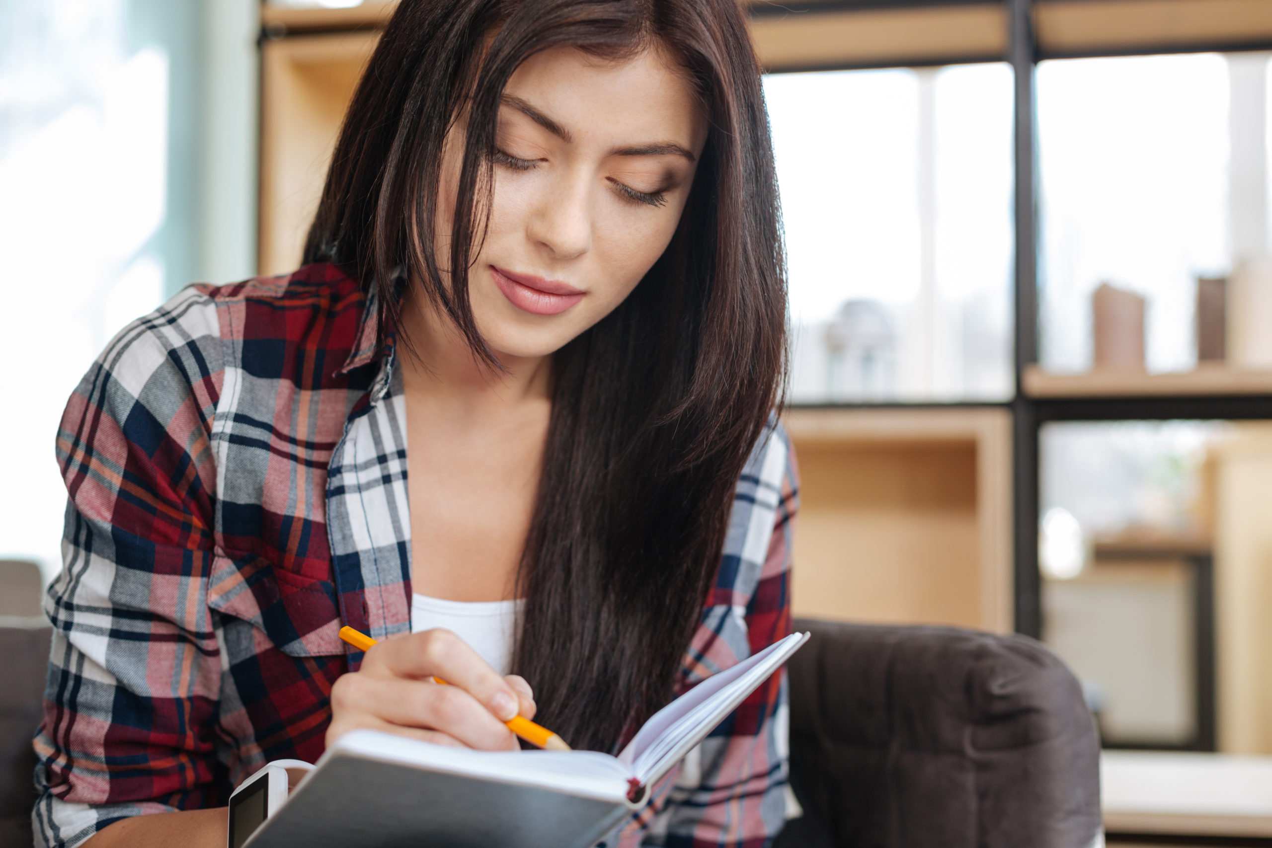sudden-inspiration-beautiful-creative-brunette-woman-holding-a-notebook-and-writing-in-it-while-being-concentrated-on-the-activity-stockpack-istock