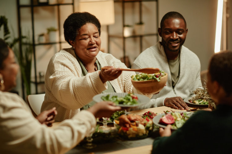 Portrait of smiling African-American grandmother serving food while celebrating Thanksgiving with big happy family at dinner table