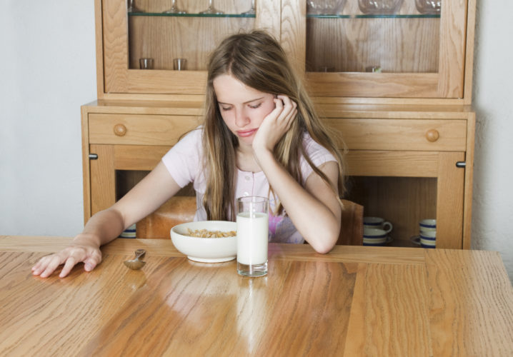 young beautiful teenager looking at a plate of cereal with an attitude of dislike