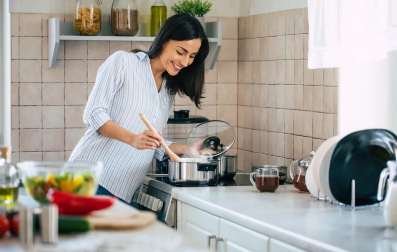 Beautiful happy young woman is cooking in the home kitchen and testing some soup from the pan on the stove