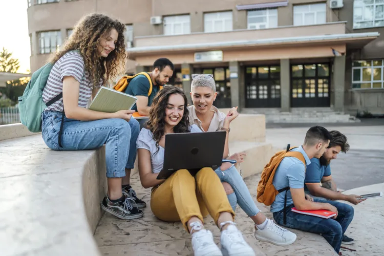 Group of students sitting outdoors, hanging out, talking and using laptop