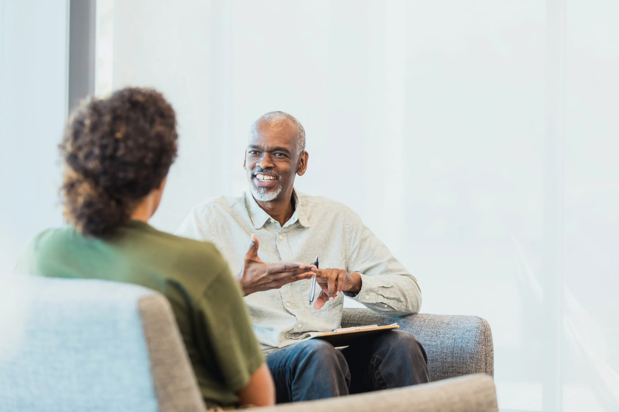 An unrecognizable mid adult woman listens as the cheerful mature adult male counselor gestures and speaks.