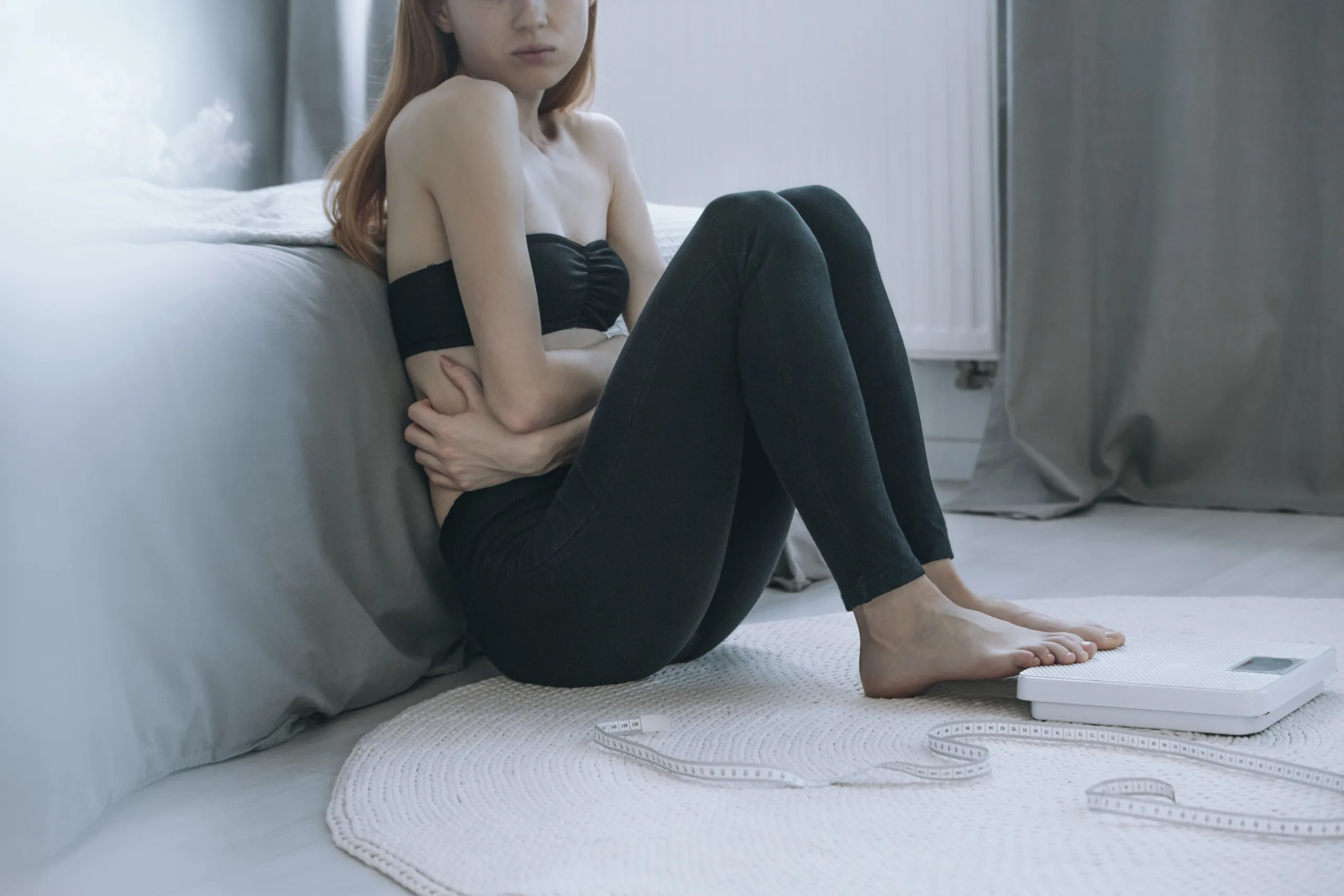 Close-up of young sick girl with stomach pain sitting on white carpet with foot on balance