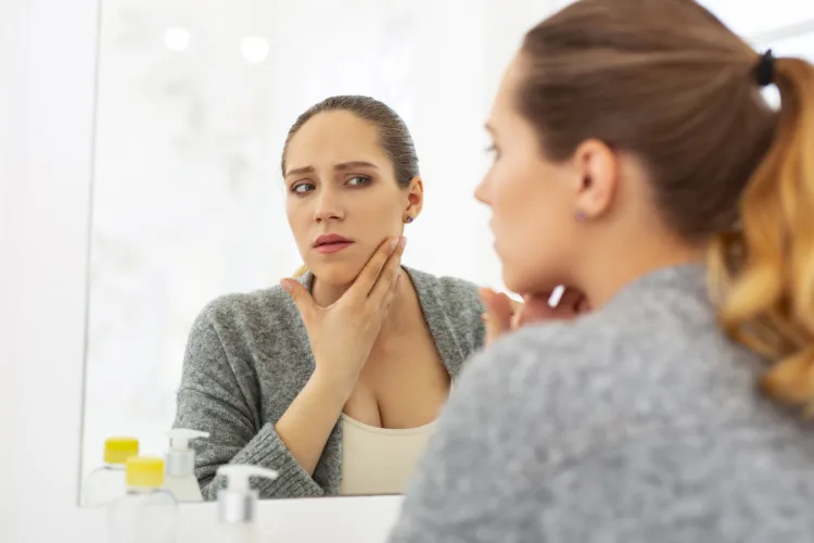 Common problem. Uneasy worried woman looking at mirror and putting hand on neck