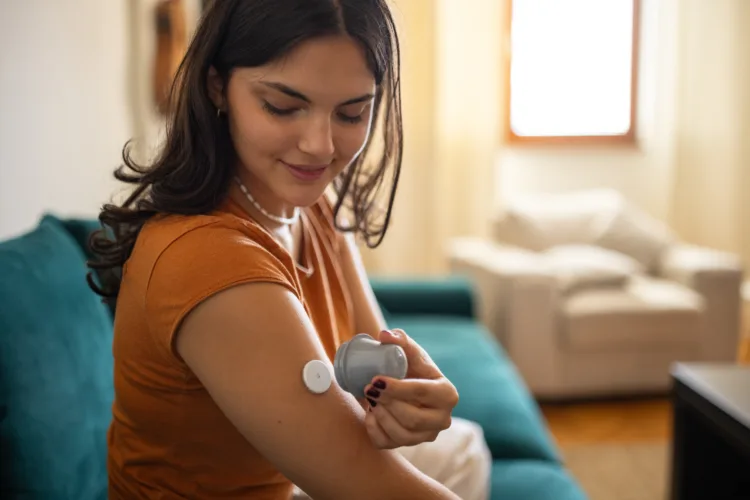 Young diabetic patient teenage woman using applicator to attach glucose sensor on arm.
