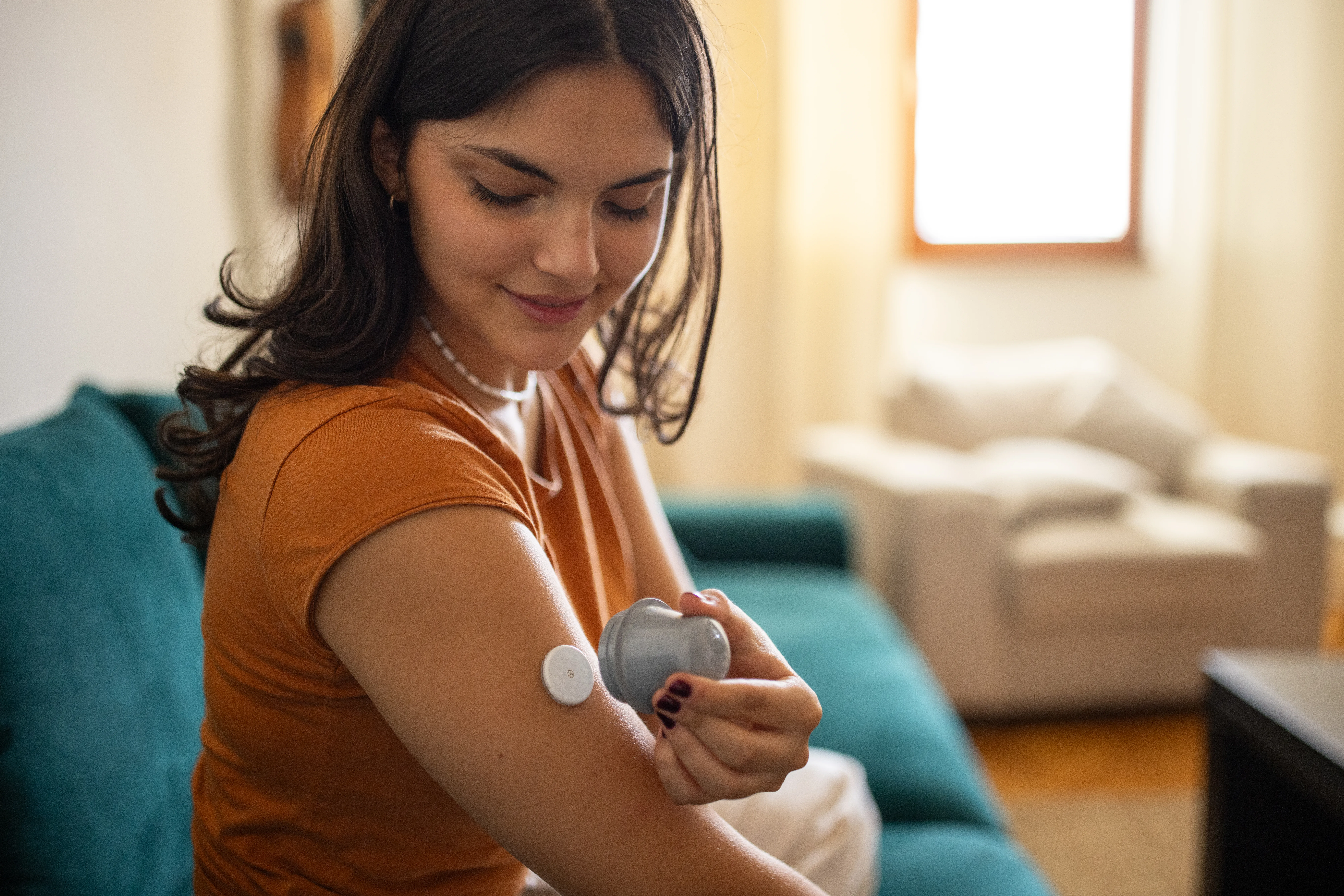 Young diabetic patient teenage woman using applicator to attach glucose sensor on arm.