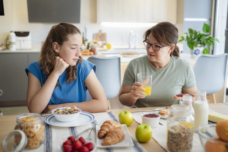 Mother and distraught teenage daughter having breakfast together and mother is noticing that her daughter isnt eating