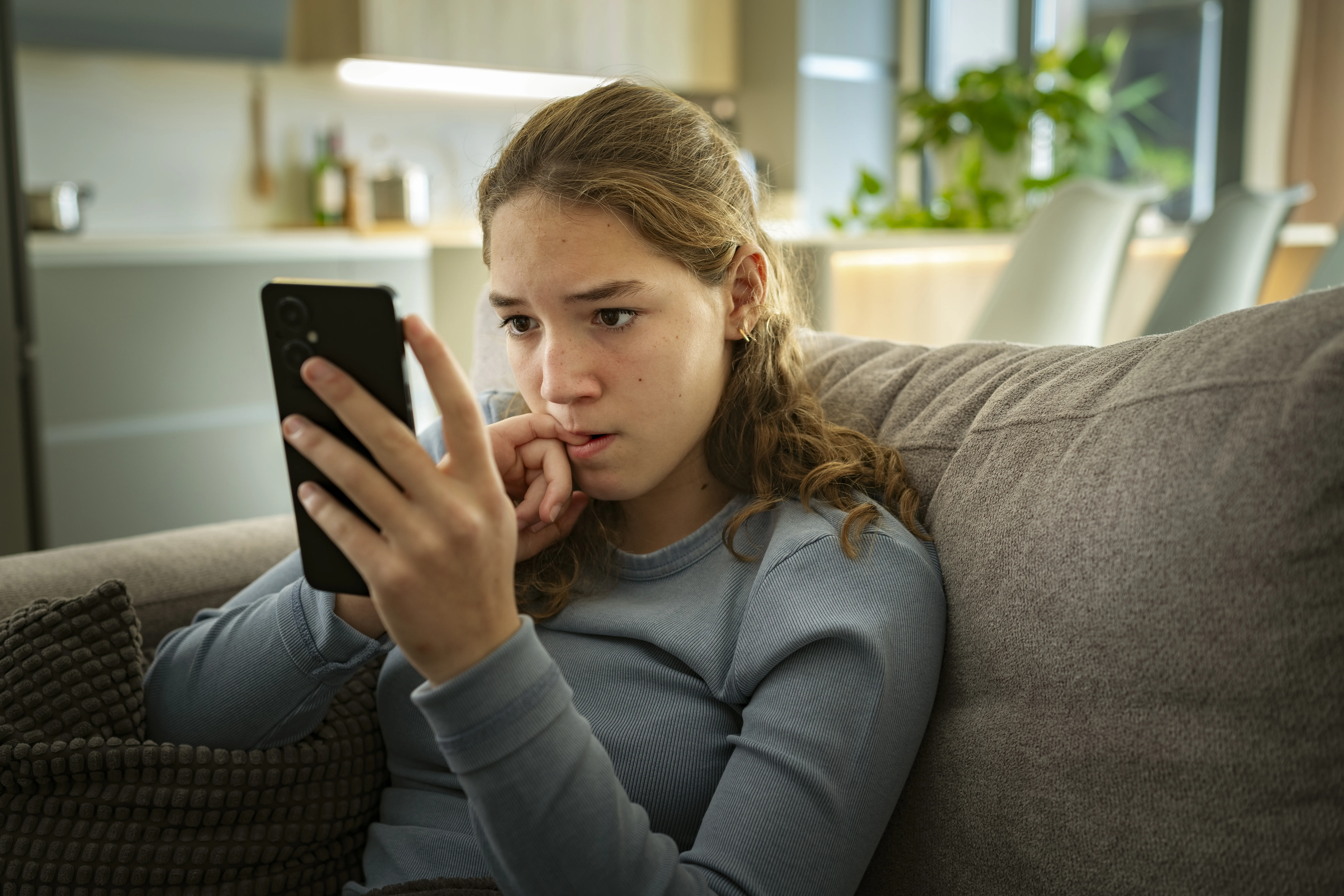 Portrait of a nervous teen girl looking at her smartphone biting her nails while watching skinnytok