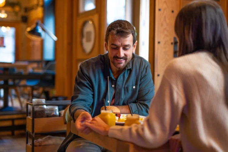 Shot over the woman's shoulder of couple sitting in the restaurant having lunch, holding hands, this is the moment of silence, the man looks insecure, hesitate to say something.