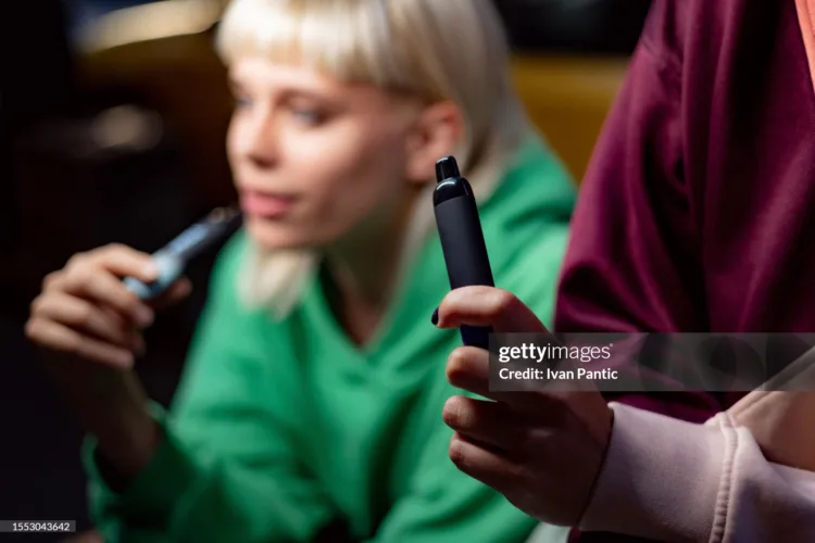 Close up of unrecognizable woman smoking electronic cigarette with her friend.