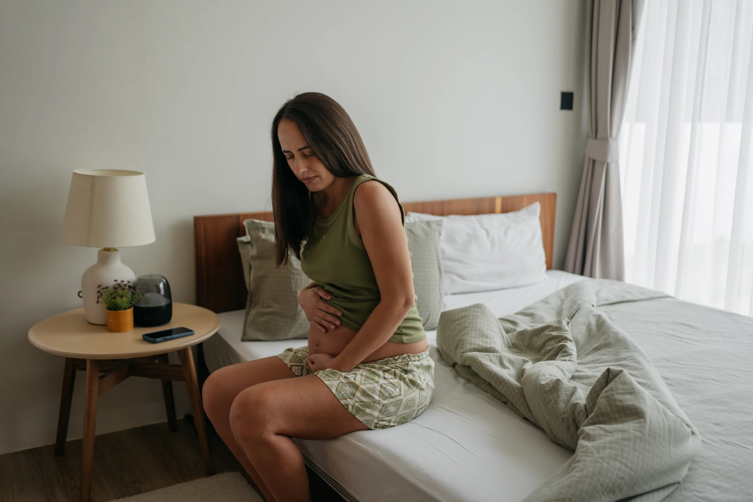 Pregnant woman is holding her belly with a pained expression on her face as she feels the signs of hunger.