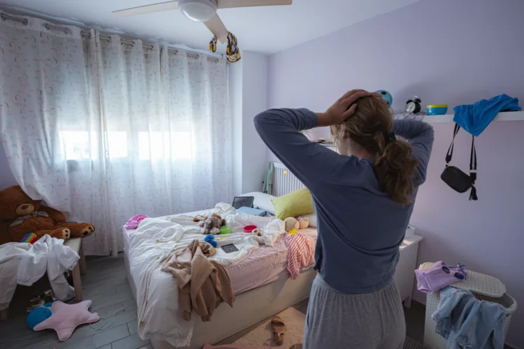Teenager girl head in hands looking shocked her messy bedroom