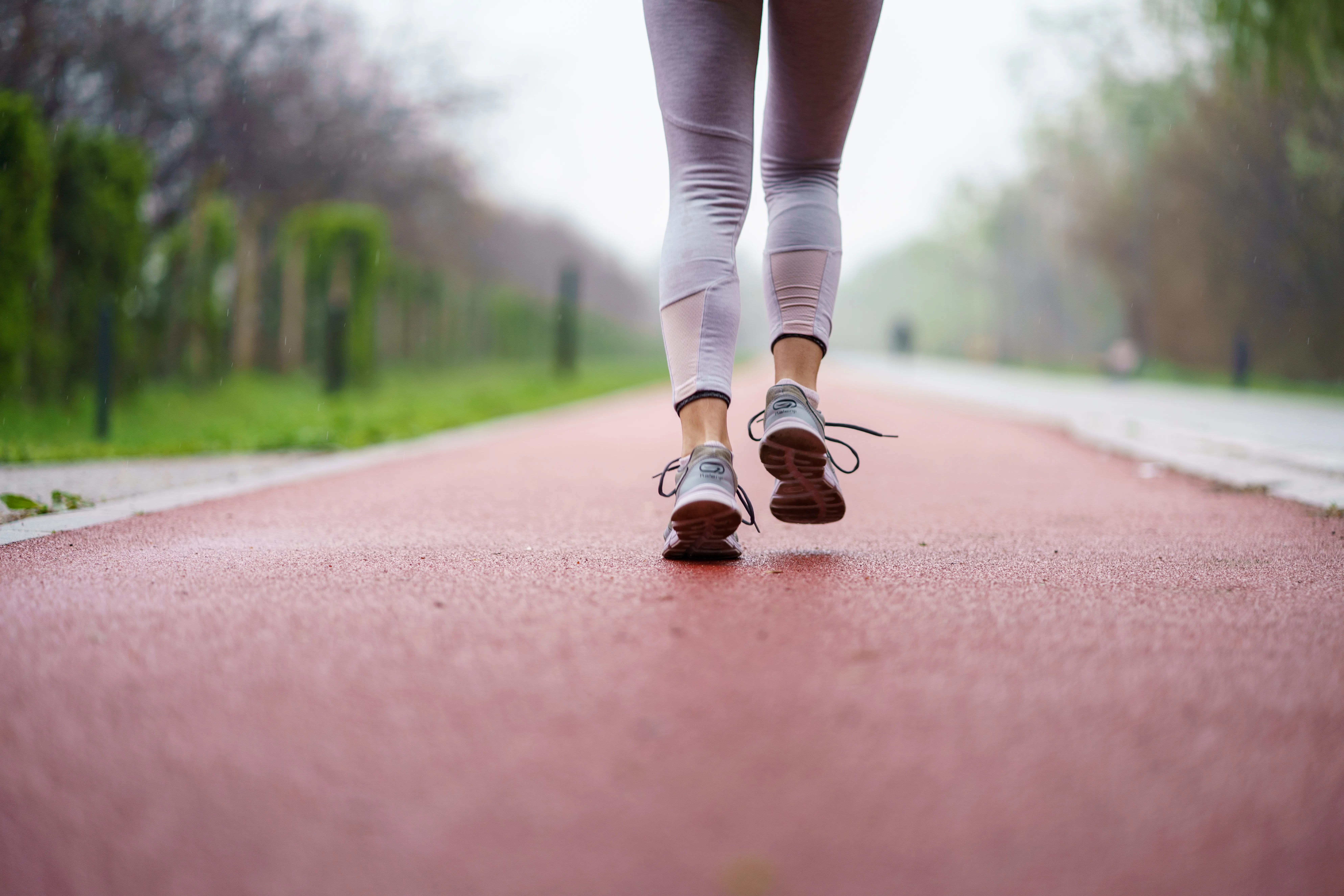 Close up of a woman runs outdoors on a wet red track in leggings