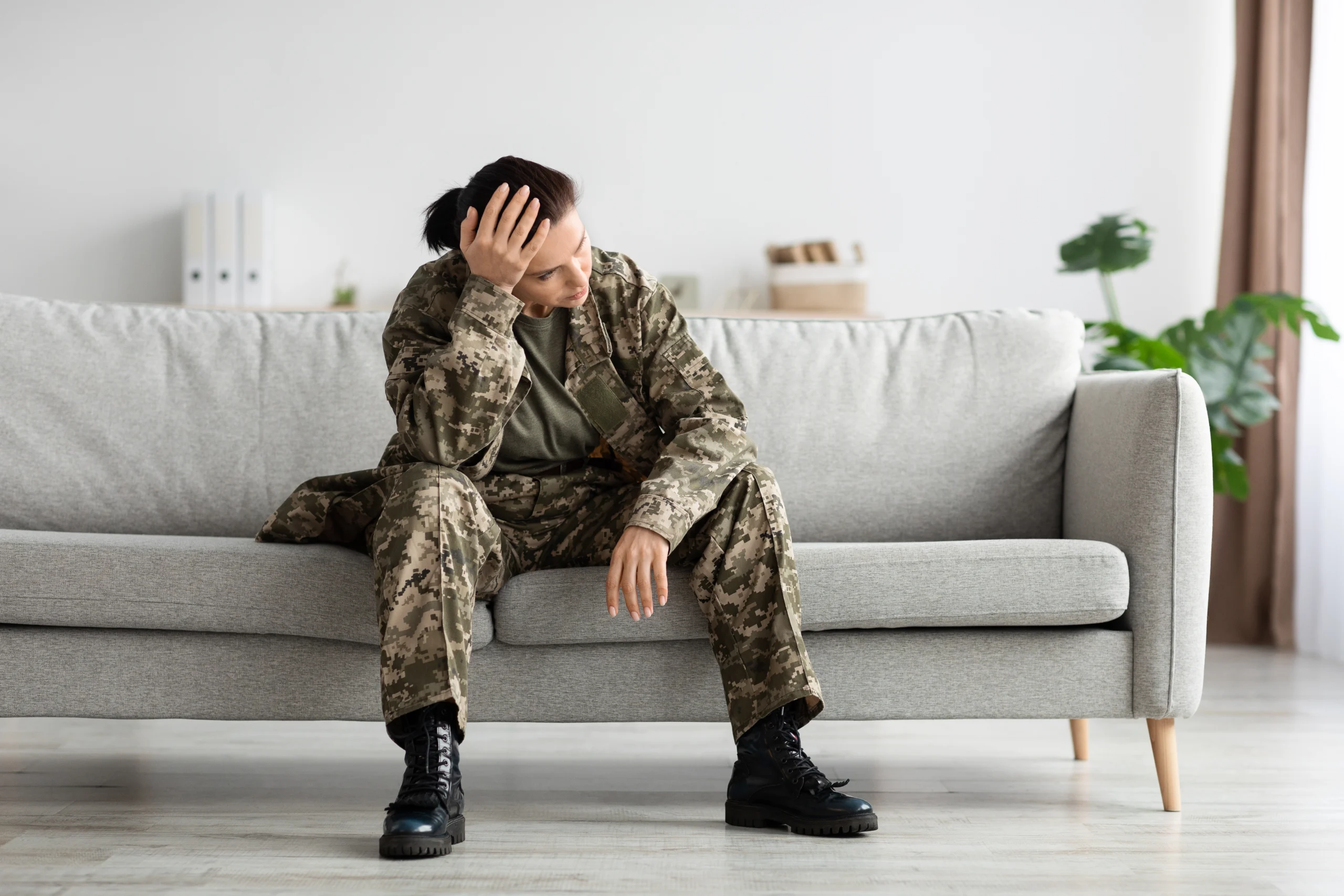 Mental Disorders In Military. Depressed Soldier Lady In Uniform Sitting On Couch Indoors, Portrait Of Pensive Upset Army Woman Wearing Camouflage Touching Head And Looking Away, Copy Space
