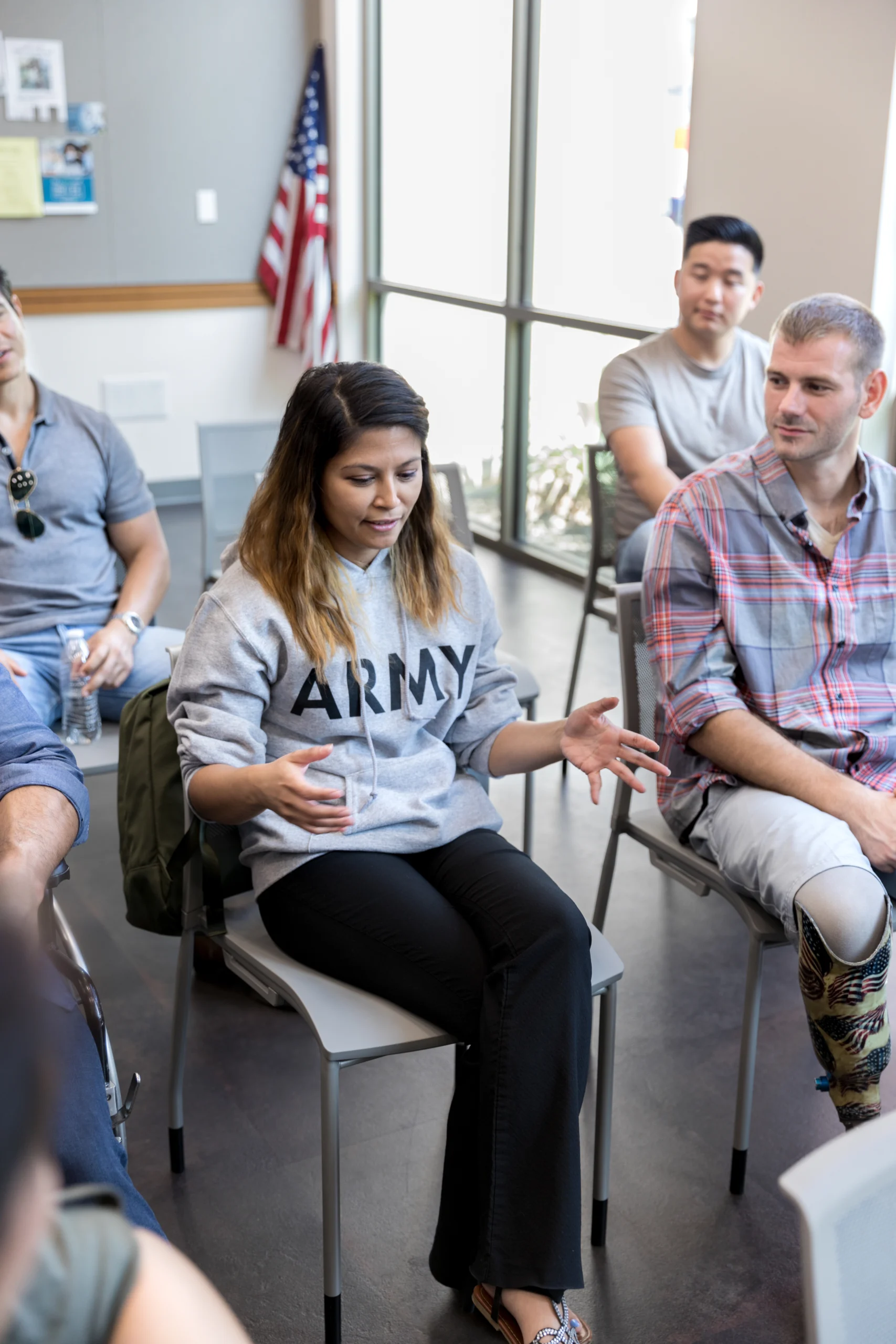 With fellow veterans looking on, the mid adult female veteran gestures as she speaks.